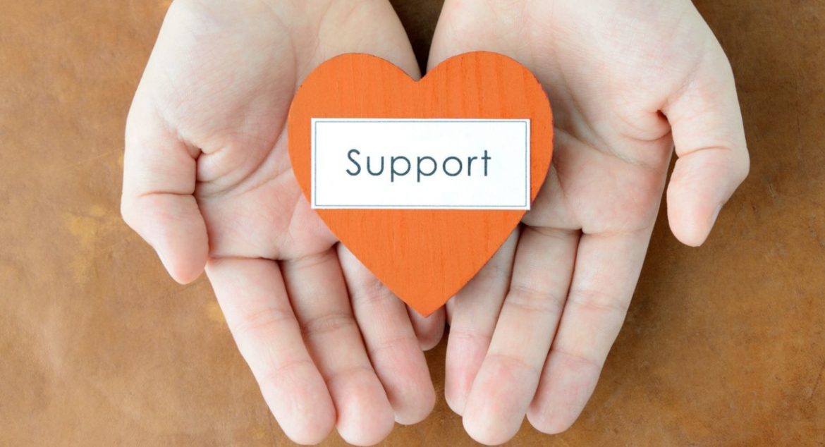 Hands holding a wooden heart that reads "support"