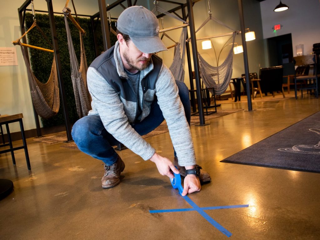 K Brew CEO Pierce LaMacchia tapes an "X" on the floor to mark proper social distancing inside the coffee shop’s West Hills location