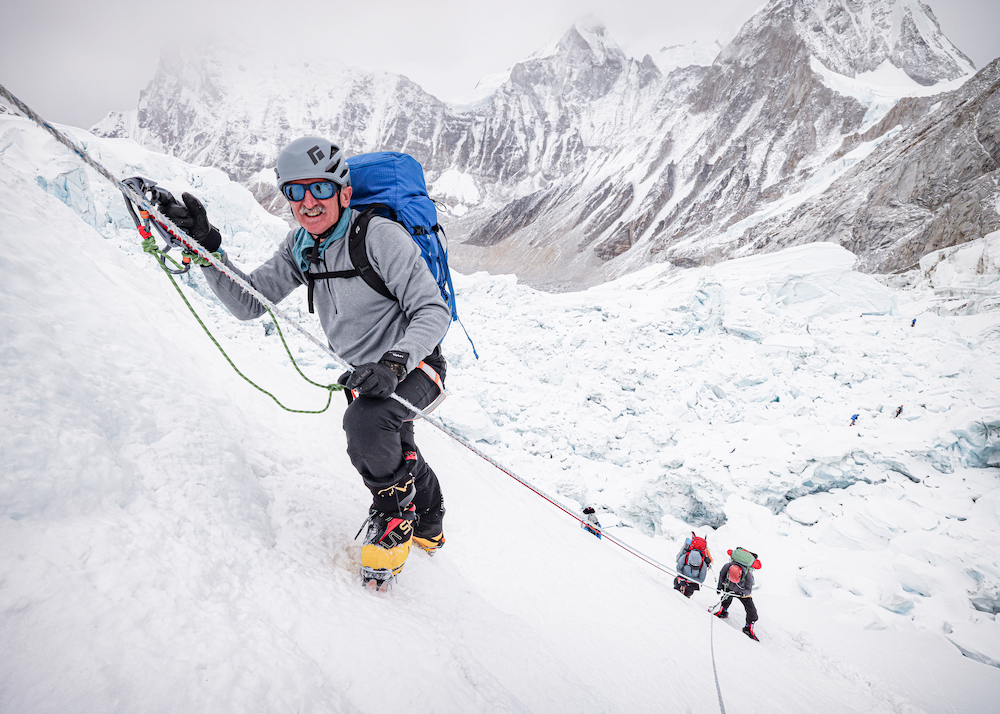 Lonnie Bedwell holds onto a large cable as he scales Mount Everest.