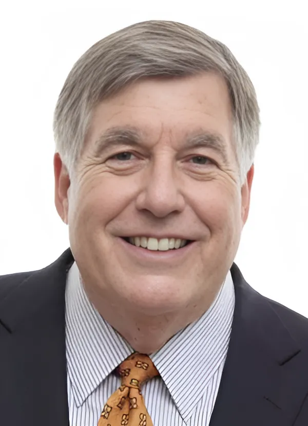 Portrait of Bob Kesling—an older man with light skin and short gray hair—wearing a striped button-down shirt, an orange tie, and a black blazer, against a white background.